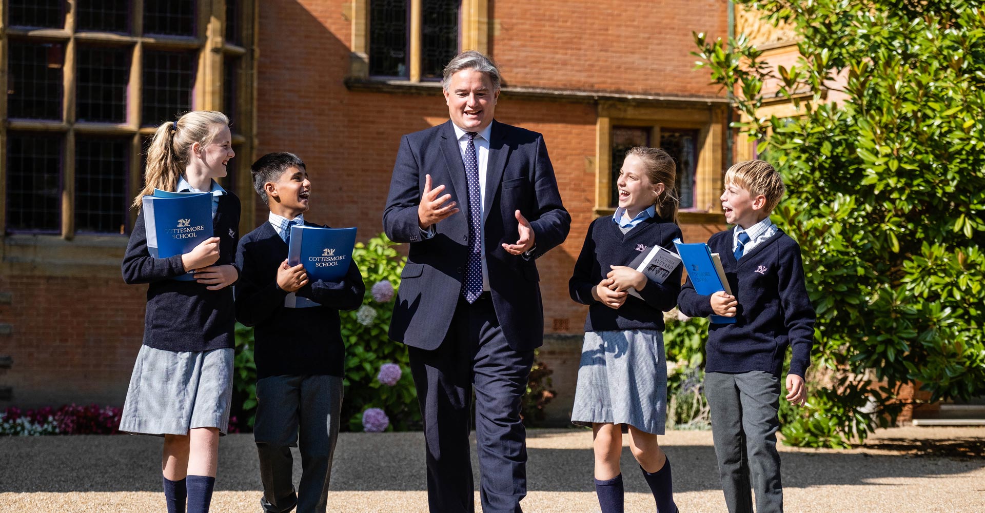 cottesmore school teacher conversing with happy pupils in uniform outside carrying books