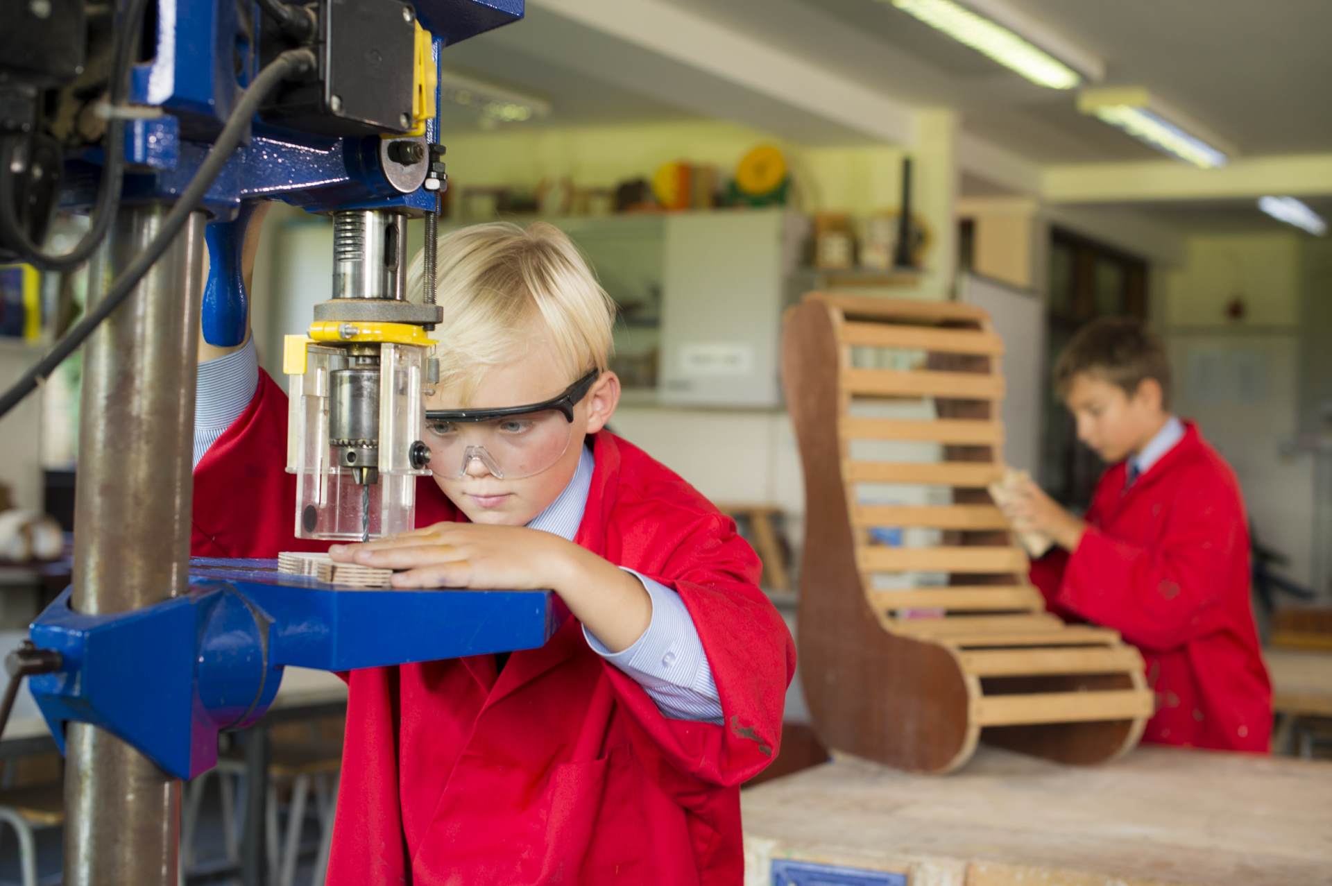 cottesmore school male pupils in red overalls safety goggles glasses practicing design technology sanding drilling woodwork