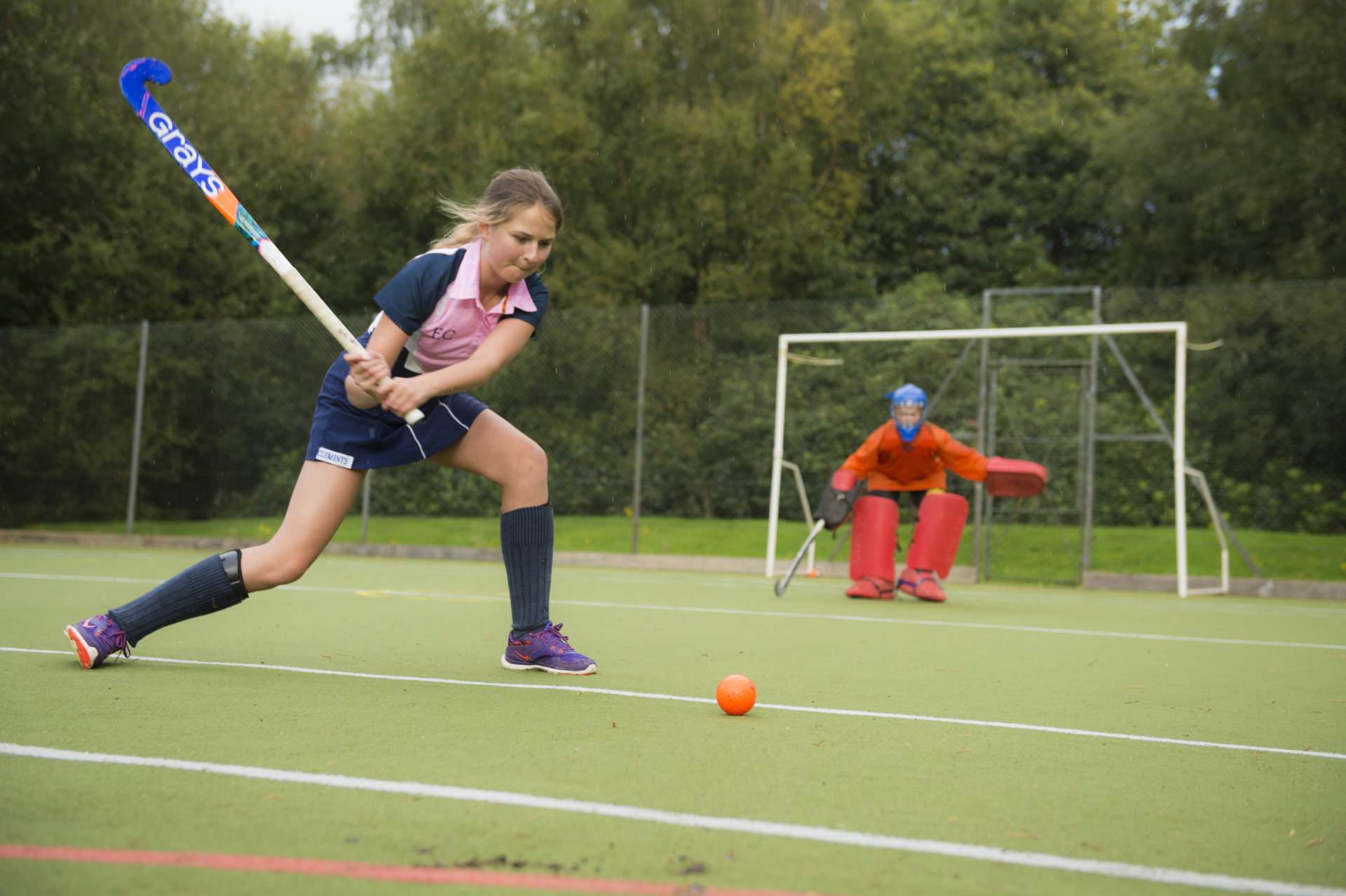 cottesmore school female pupil attempt to score a goal playing hockey on pitch with goalie in red in background