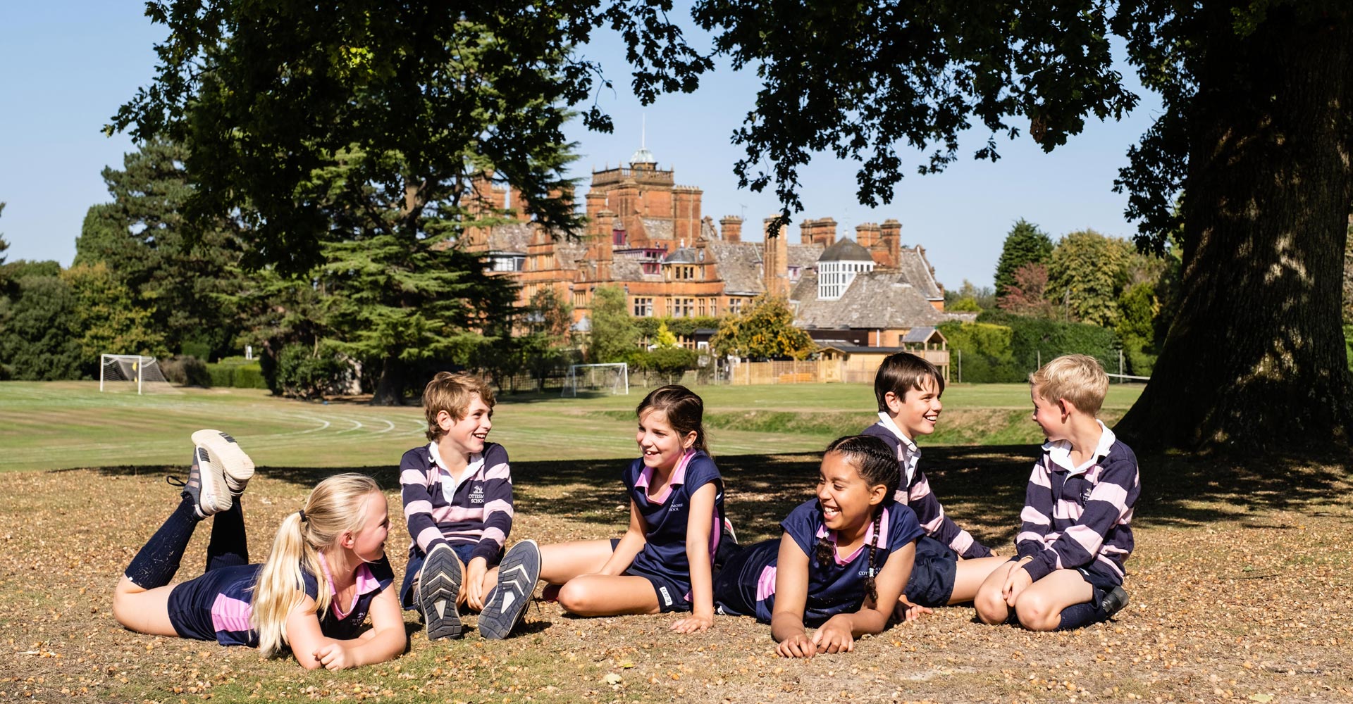 cottesmore school pupils sitting laying on ground outside under oak tree in rugby hockey kit uniform