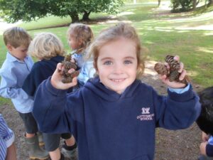 cottesmore school pupils standing outside holding pinecones in navy hoodies light blue shirts exploring