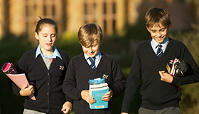 cottesmore school pupils in uniform light blue shirts black cardigan jumpers walking outside carrying books and pencil cases