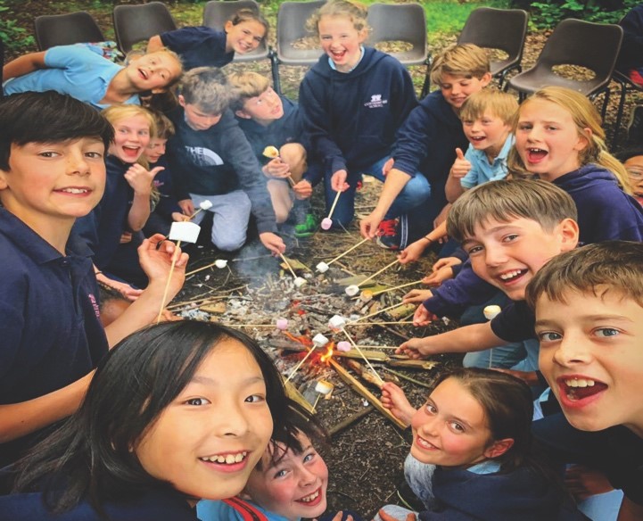 cottesmore school pupils sitting around campfire toasting marshmallows all smiling at camera